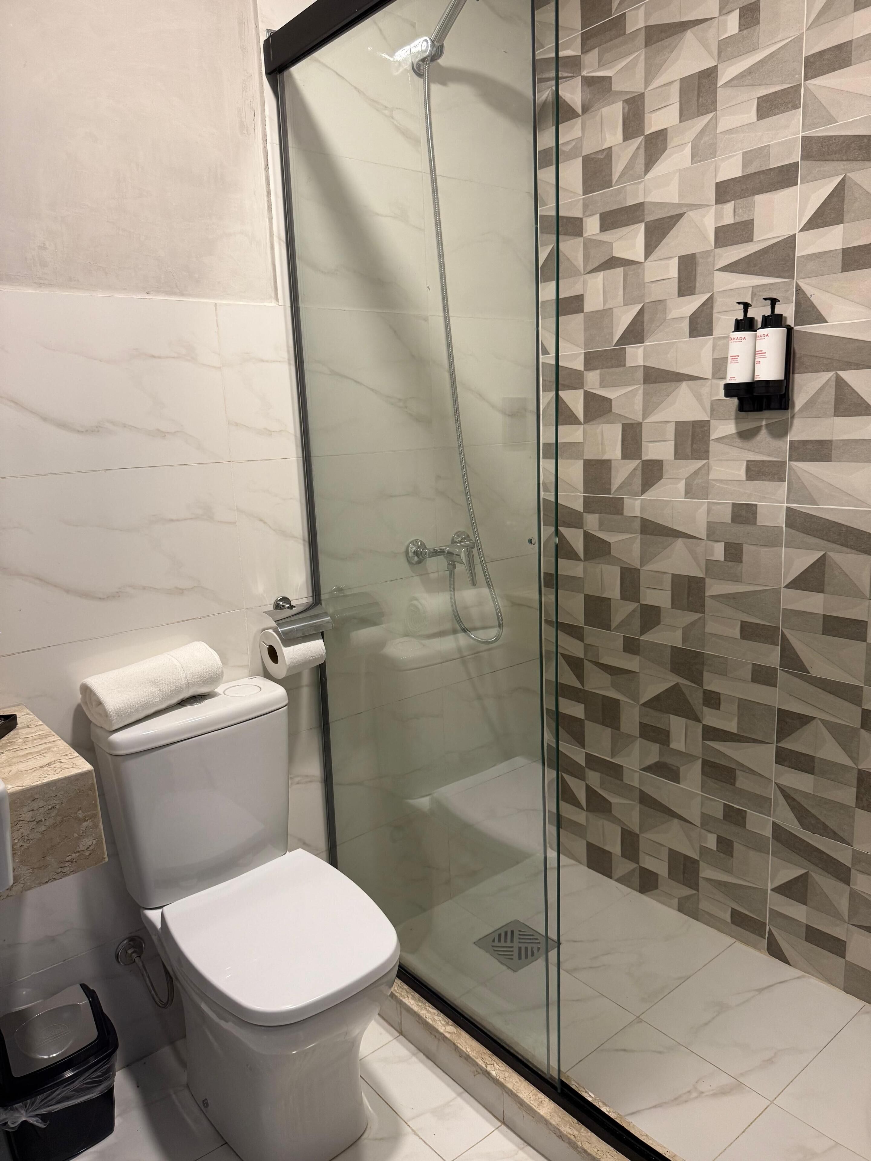 A modern bathroom with a glass-enclosed shower, a toilet, and a patterned wall.
