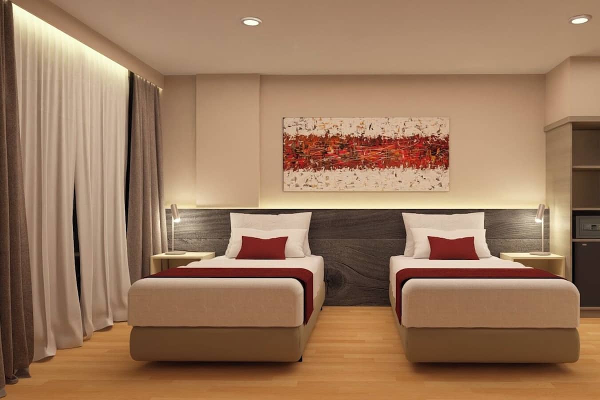 Quarto de hotel com duas camas, uma grande pintura abstrata, um guarda-roupa e uma escrivaninha com abajur.