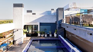 A rooftop pool with a clear view of the surrounding landscape, a modern building with large windows, and potted plants along the pool's edge.