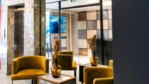 A lobby with yellow chairs, a marble column, and a glass door leading to a room.