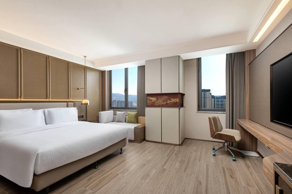 Une chambre d’hôtel avec un grand lit, un bureau avec une chaise, une télévision et une vue sur la ville.