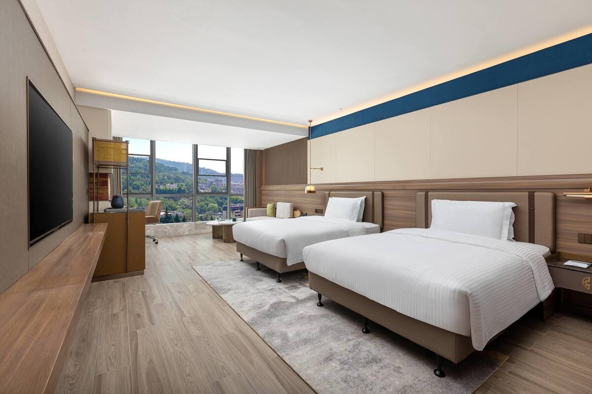 Une chambre d’hôtel moderne avec deux lits, un bureau et une grande fenêtre donnant sur la ville.