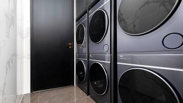 A laundry room with four stacked front-loading washing machines, a black door, and a marble-tiled floor.