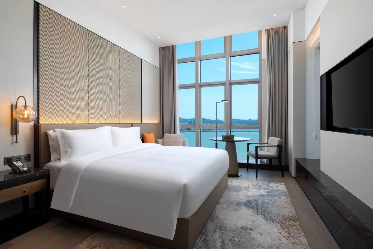 A modern hotel room with a large bed, a desk with a telephone, a round table, and a TV.