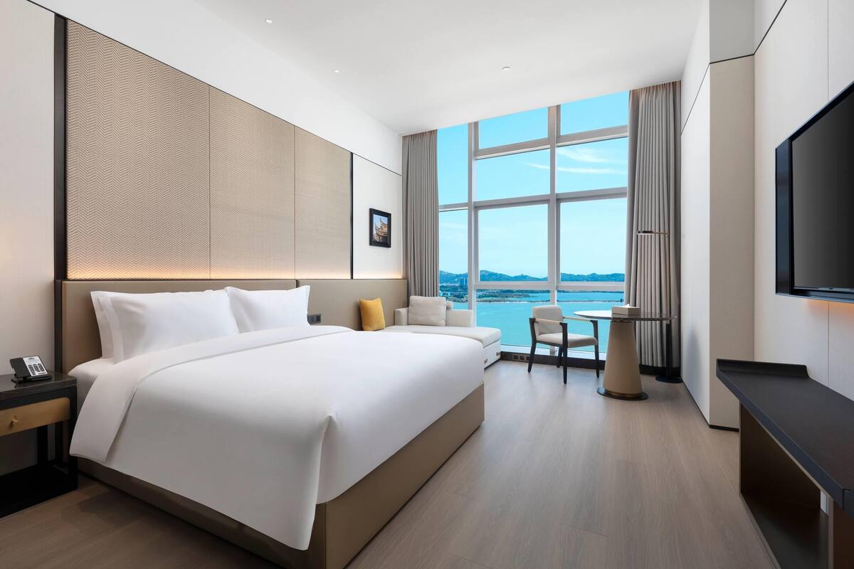 A modern hotel room with a large bed, a desk, a chair, and a TV.