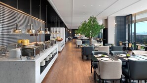 Un restaurante moderno con una barra alargada, varias zonas de estar y un amplio ventanal con vistas a la ciudad.