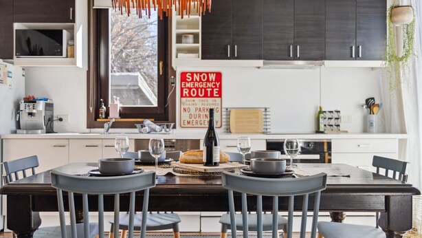 Une cuisine moderne avec une table à manger pour deux, une machine à café et un panneau indiquant un itinéraire de déneigement en cas d’urgence.