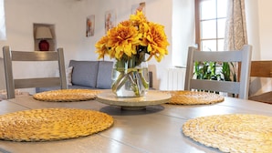 A dining table with woven placemats, a clear vase with yellow flowers, and a lamp in the background. - Cosy gîte with view, jacuzzi & pool - heart of the Cévennes, hiking, relaxation. (Ventalon en Cévennes)
