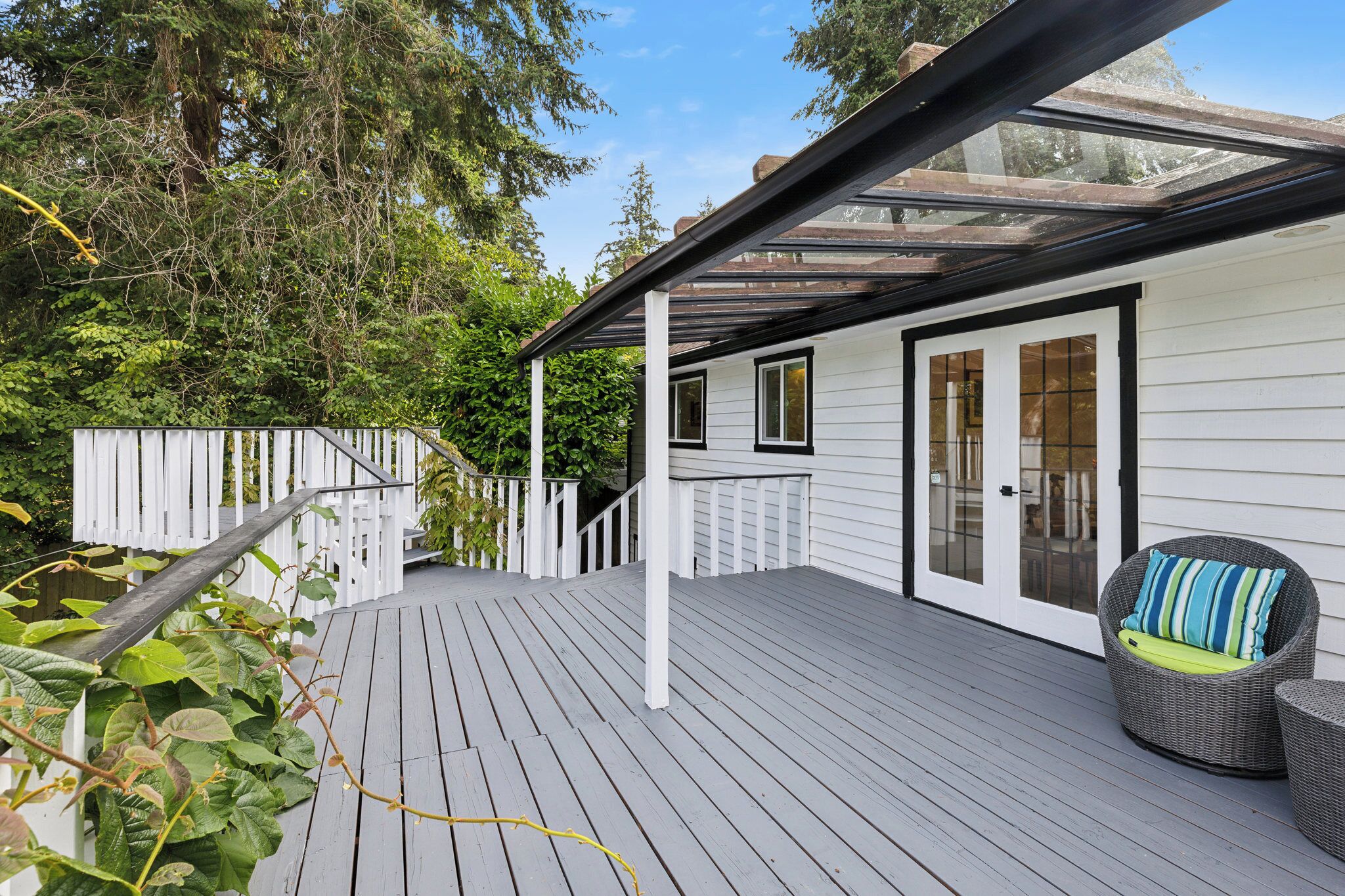 A wooden deck with a glass enclosure, white exterior walls, and a wicker chair with a cushion.