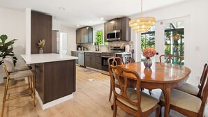 A modern kitchen with a central island, wooden dining table, and bar stools.