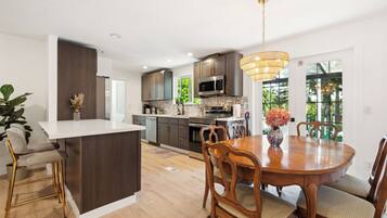 A modern kitchen with a central island, wooden dining table, and bar stools.