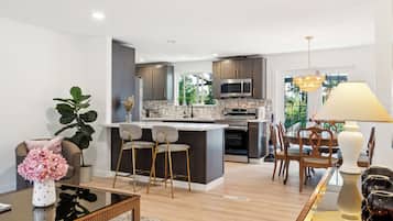 A modern kitchen with dark cabinets, a central island, and a dining area with wooden chairs and a table.