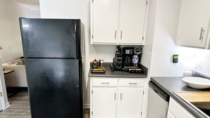 A kitchen with a black refrigerator, white cabinets, and a coffee maker on the countertop. - Newnan Gem (Newnan)