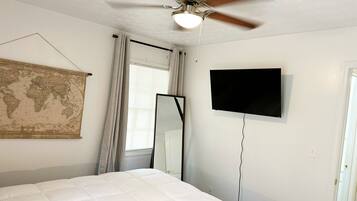 Une chambre à coucher avec un lit, un ventilateur de plafond, une carte du monde, un téléviseur et une fenêtre avec des rideaux.