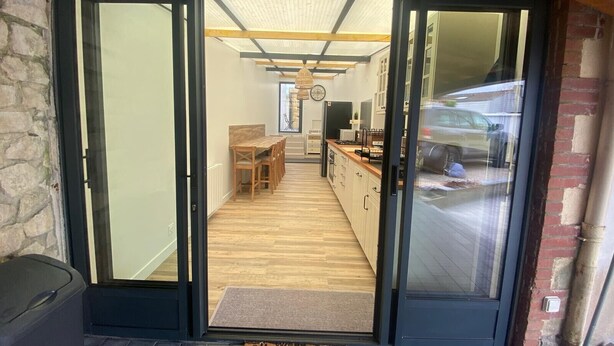 A modern kitchen with a wooden table and cabinets, a visible stove, and a large window. - CHEZ MIMI - Holiday home (Jard-sur-Mer)