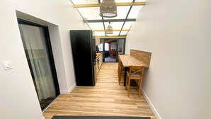 A narrow hallway with a wooden floor, a black refrigerator, a dining table with chairs, and a hanging light fixture. - CHEZ MIMI - Holiday home (Jard-sur-Mer)