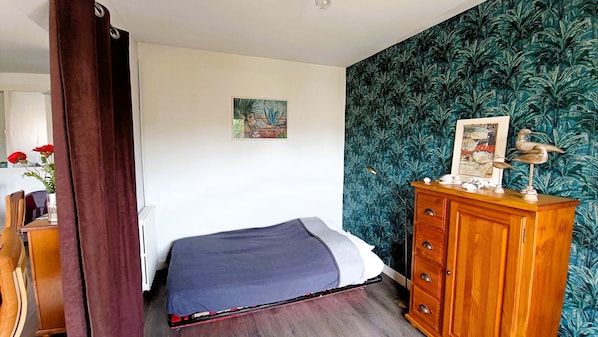 A bedroom with a bed, a wooden dresser, a painting on the wall, and a tropical wallpaper. - LE ROCHEFORT - 4/6 personnes (Les Sables-d´Olonne)