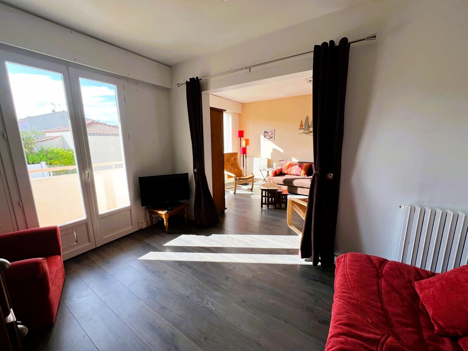 Een ruime woonkamer met een grote televisie, een rode bank en een houten vloer.