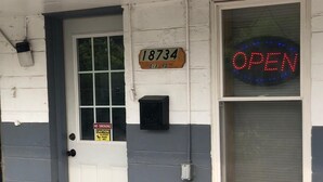 A building with a white door, a 'NO SMOKING' sign, a 'Caution: Slippery When Wet' sign, and a neon 'OPEN' sign.