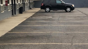 Un estacionamiento con una hilera de edificios de una sola planta, una camioneta SUV negra estacionada y una pared azul y amarilla al fondo.