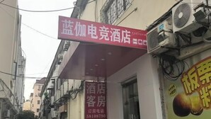 Une rue étroite bordée d’un hôtel et d’une maison d’hôtes. On y voit des panneaux indiquant l’hôtel et la maison d’hôtes, et un grand appareil de climatisation est visible sur le bâtiment.