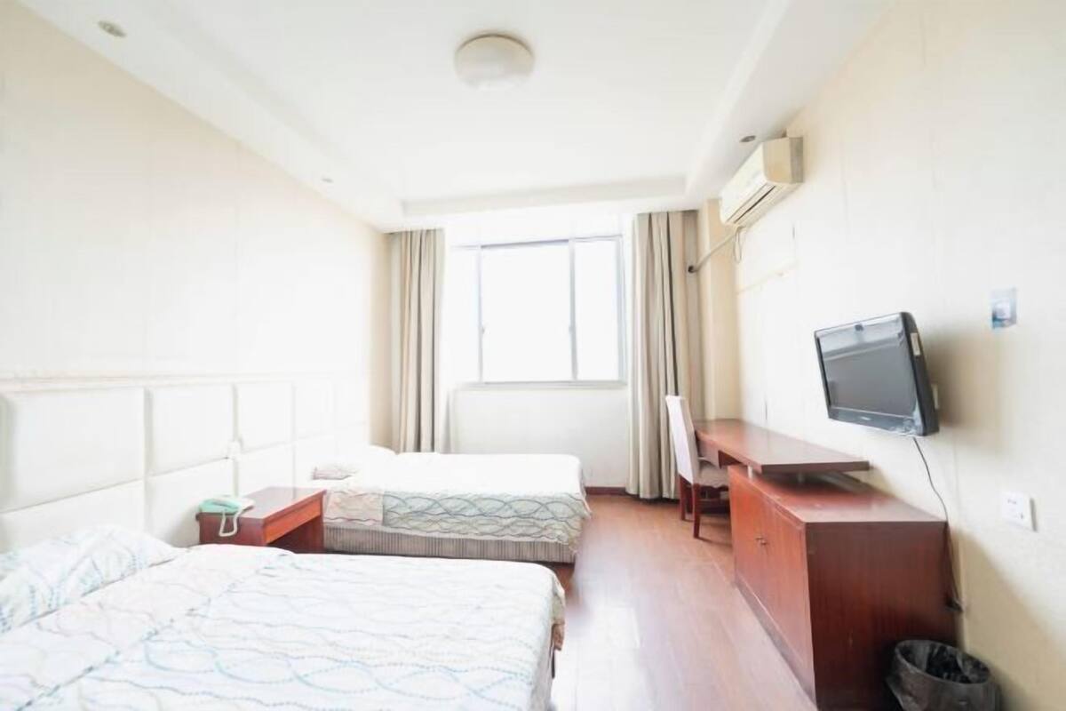 Een hotelkamer met twee bedden, een bureau, een televisie en een raam.