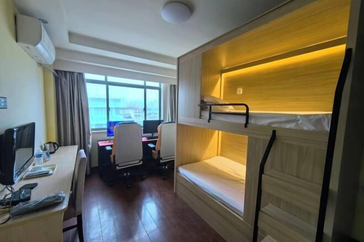 Een hotelkamer met een stapelbed, een bureau met een computer, een stoel en een raam met uitzicht.