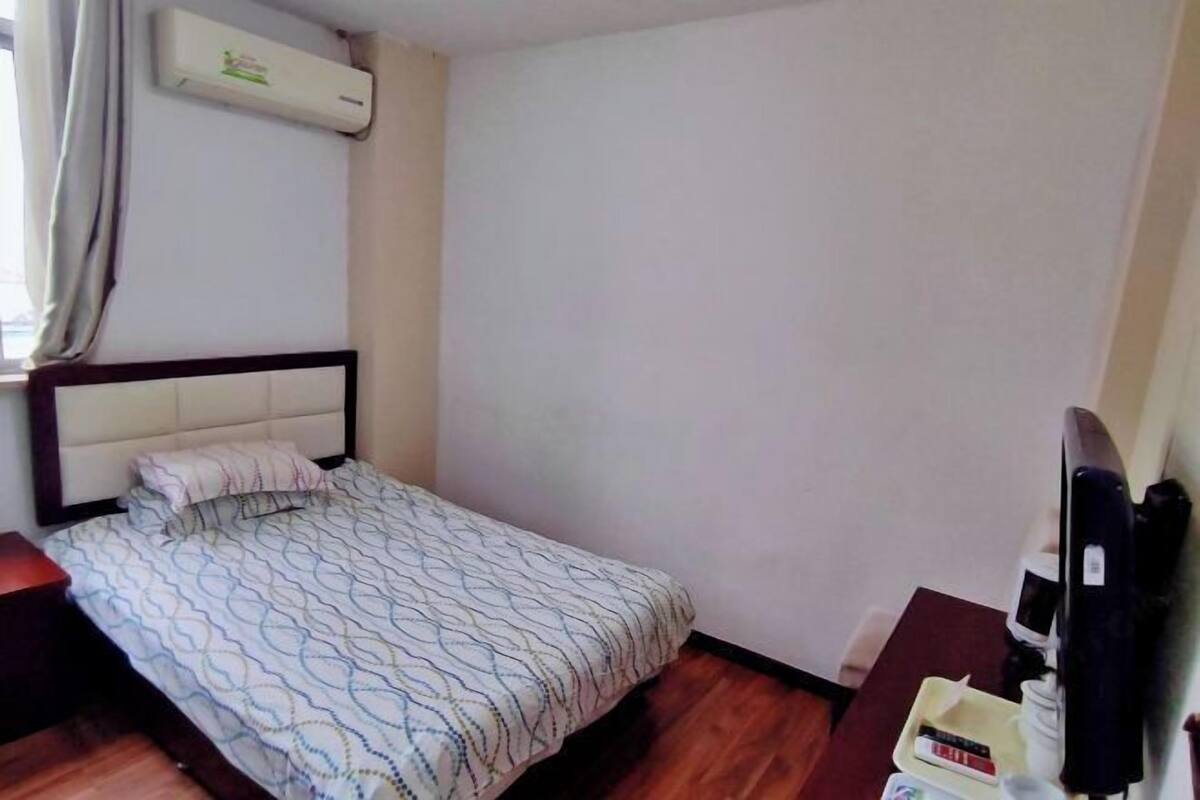 Een eenpersoonsbed met een bedekt met een patroon, een nachtkastje met een afstandsbediening en een airconditioner aan de muur.