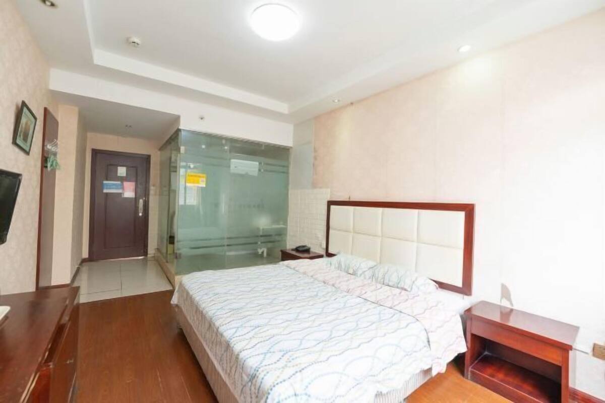 Een hotelkamer met een groot bed, een houten bureau en een glazen scheidingswand.