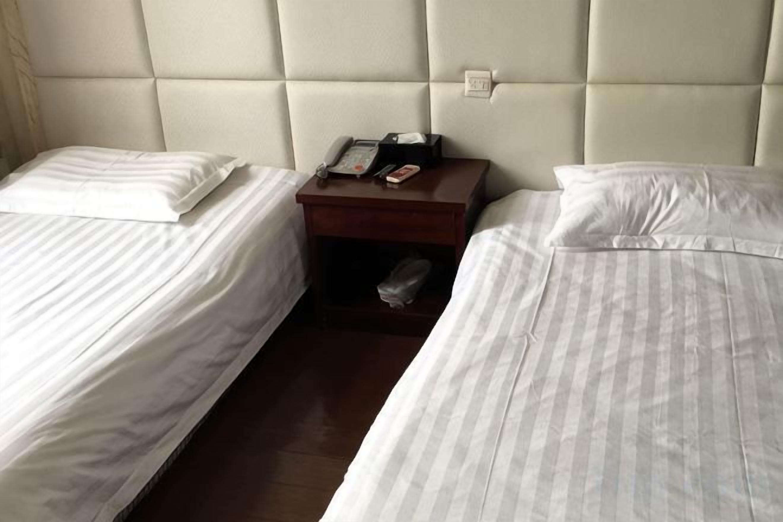A hotel room with two beds, a bedside table with a phone, and a small shelf.