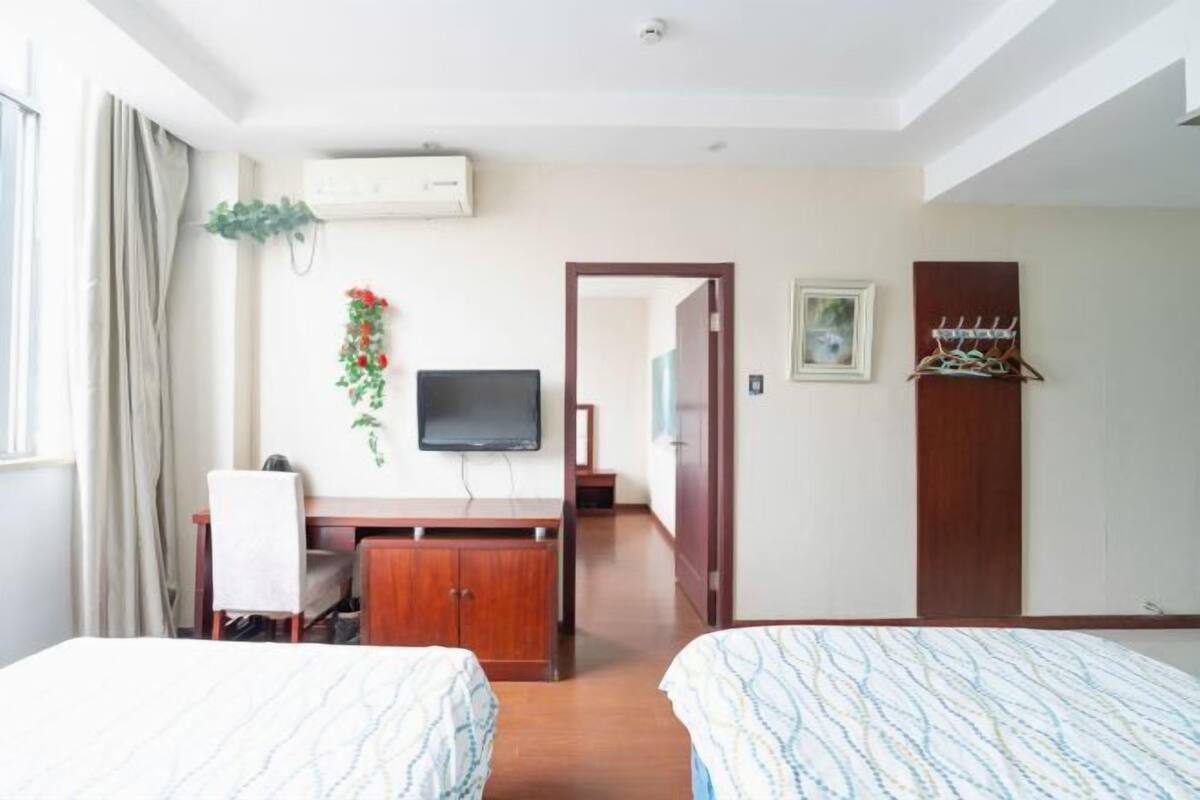 Een hotelkamer met twee bedden, een bureau, een televisie, airconditioning, een deur en een kapstok.