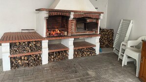 Udendørs pizzoven i mursten med skorsten, et bord og stablet brænde.