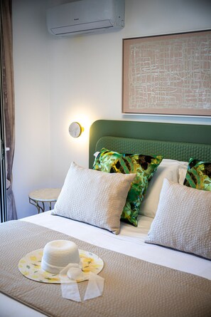 Un lit bien fait, avec une tête de lit verte, deux oreillers blancs et un chapeau décoratif posé sur un tapis à motifs floraux.