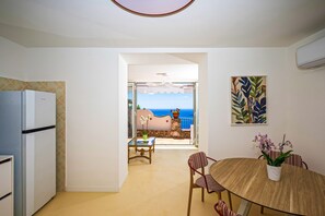 A kitchen with a refrigerator, a dining area with a table and chairs, and a view of the sea through an open door.