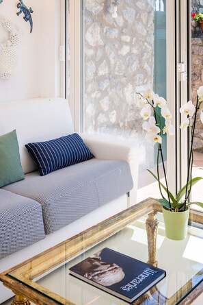 A modern living room with a white sofa, striped pillows, a glass coffee table with a book, and white orchids.