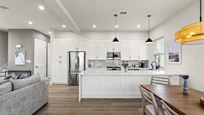 Une cuisine moderne avec des armoires blanches, des appareils en acier inoxydable et des luminaires suspendus.