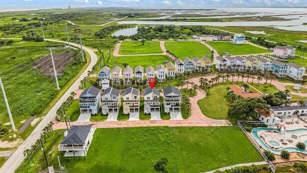 Un quartier résidentiel où les maisons sont alignées le long d’une route sinueuse, avec une piscine et une grande pelouse verdoyante.