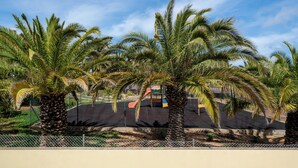 A fenced area with palm trees and a playground with a slide. - With outdoor space - Moradia Felicidade Rocha PXO (Lombas)