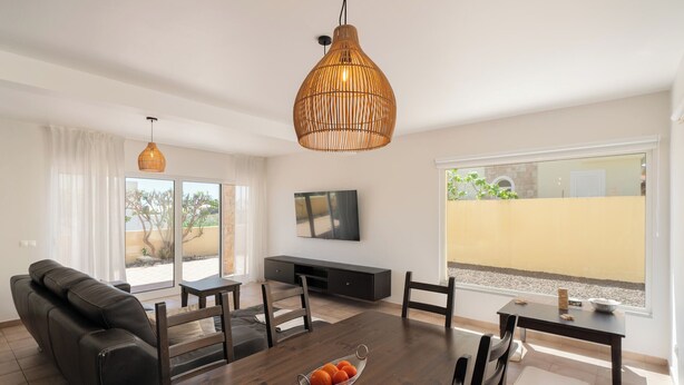 A modern living room with a wooden dining table, black leather sofa, and a large window with a view of a building. - With outdoor space - Moradia Felicidade Rocha PXO (Lombas)