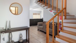 A living room with a staircase, a round mirror, and a sofa. - With outdoor space - Moradia Felicidade Rocha PXO (Lombas)