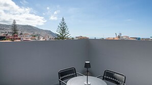 A rooftop terrace with a table and two chairs, a lamp, and a view of buildings and mountains in the background. - Quebra Costas I – A Refuge with Panoramic Views (Funchal)