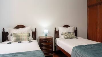 A room with two single beds, each with a wooden headboard and white bedding. There is a nightstand with a lamp between the beds.