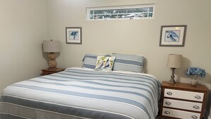 Une chambre à coucher avec un lit, deux tables de chevet, une fenêtre et deux tableaux encadrés accrochés au mur.