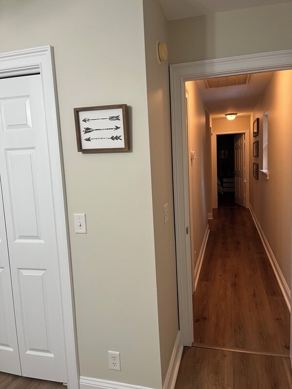 A hallway with wooden flooring, white walls, and a framed picture on the wall.