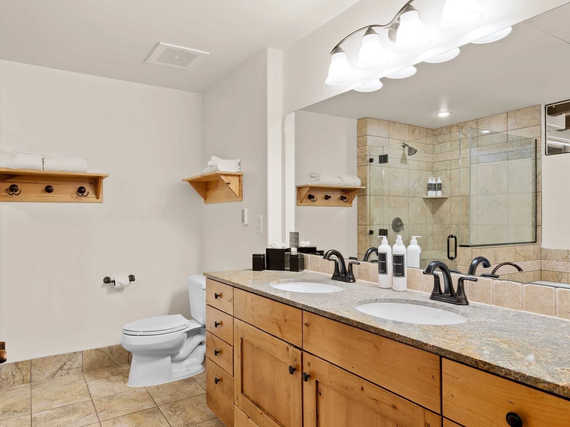 Une salle de bain moderne avec deux lavabos, des toilettes, des meubles en bois et un grand miroir.
