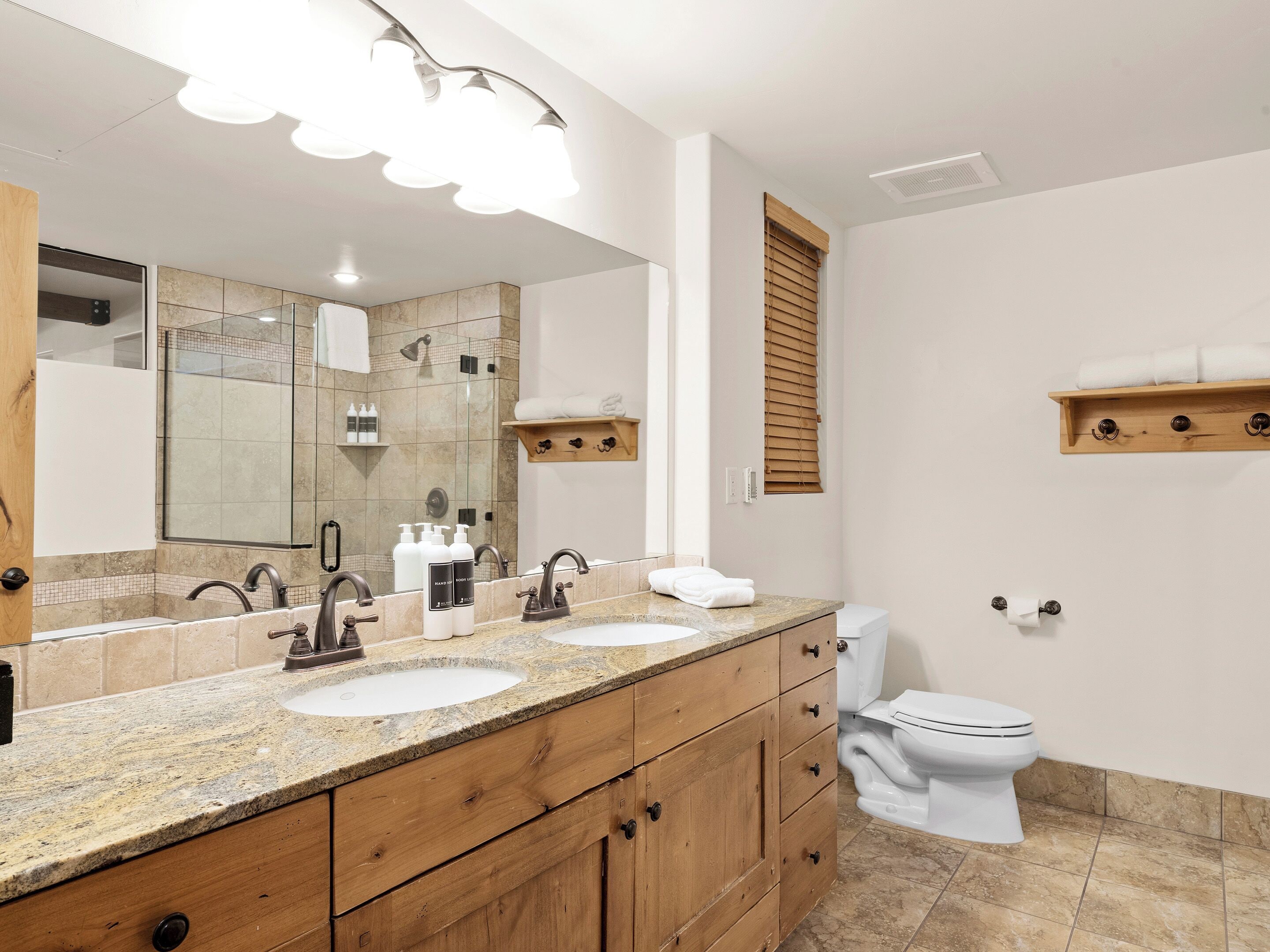 A modern bathroom with two sinks, a large mirror, and a toilet.