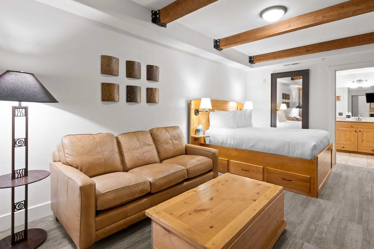 Een moderne hotelkamer met een houten bed, een leren bank, een houten bijzettafeltje en een vloerlamp.