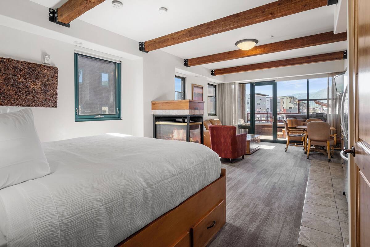 Een moderne hotelkamer met een groot bed, een open haard, een zithoek met stoelen en een balkon met uitzicht over de stad.