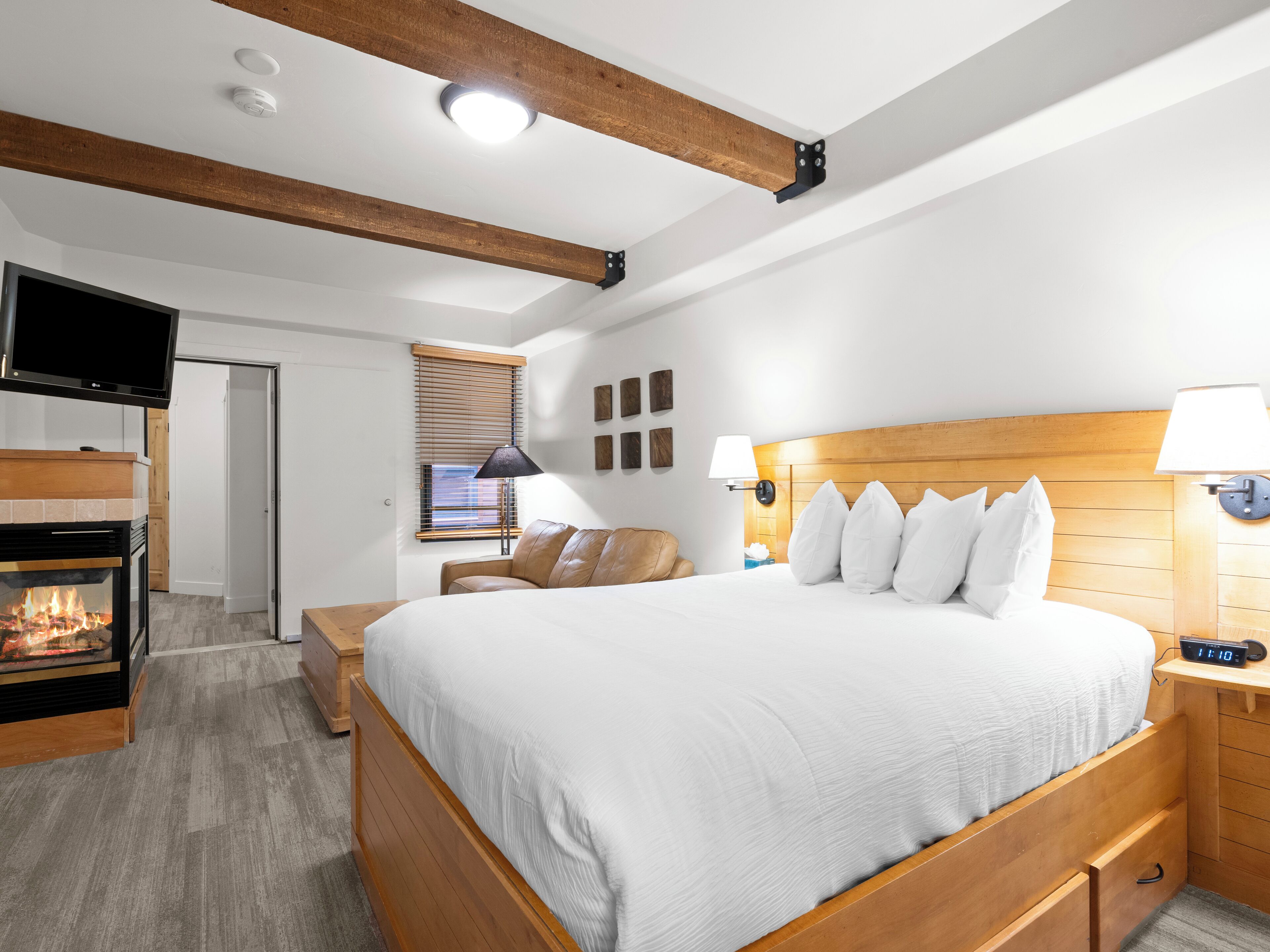 A modern hotel room with a large bed, a television, a fireplace, and a wooden ceiling.