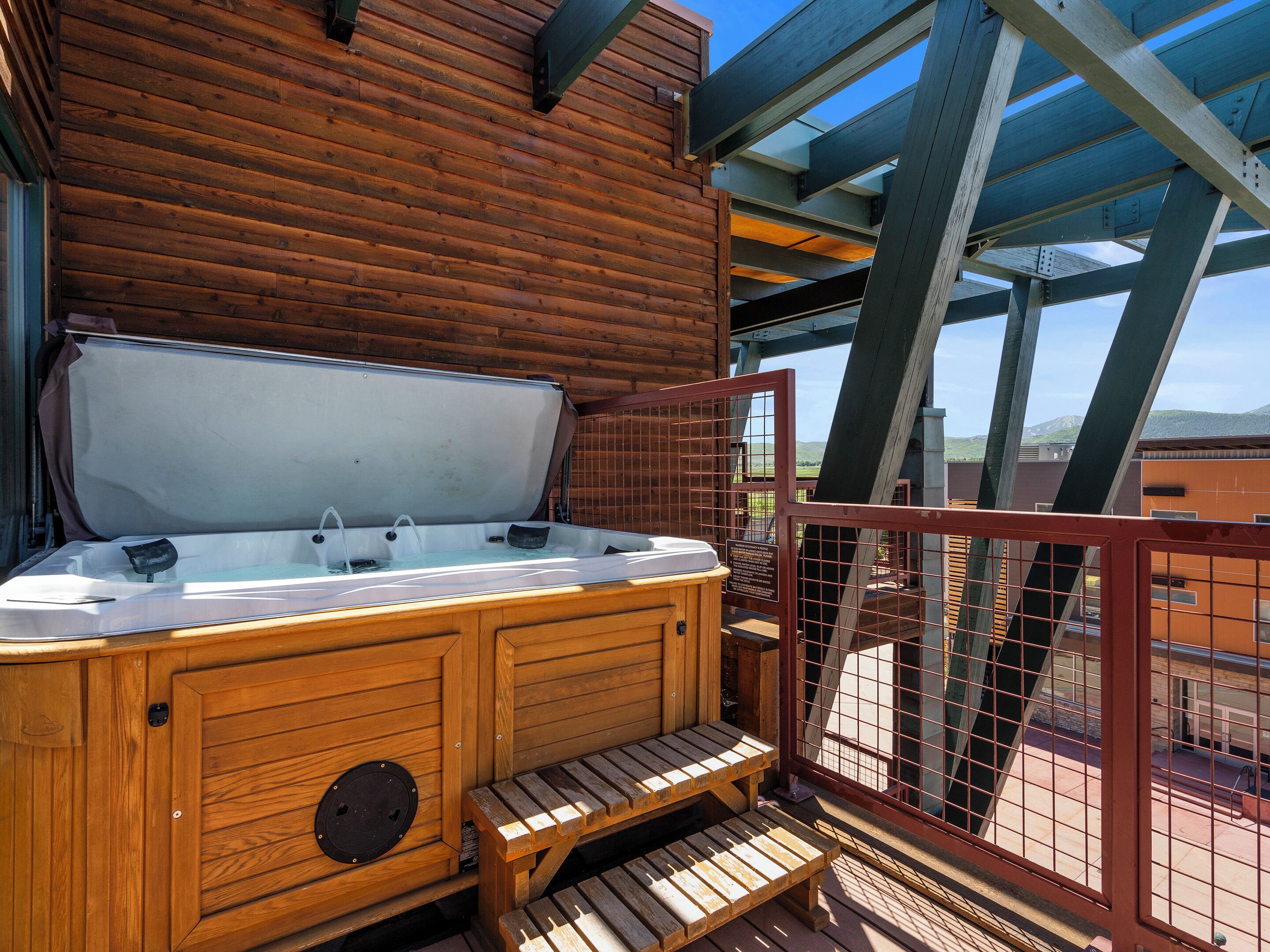 A wooden hot tub with a glass enclosure, wooden steps, and a metal railing.